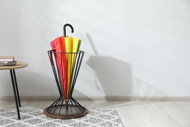 Colorful umbrella in stand near light wall. Space for text