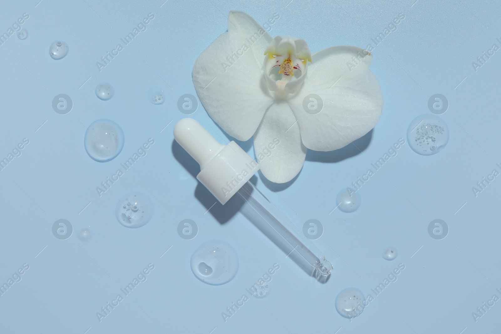 Photo of Beautiful orchid flower and dropper with cosmetic product in water on light blue background, flat lay