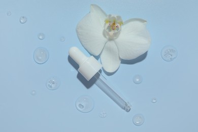 Beautiful orchid flower and dropper with cosmetic product in water on light blue background, flat lay