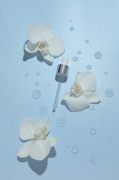 Photo of Beautiful orchid flowers and dropper with cosmetic product in water on light blue background, flat lay