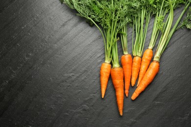 Photo of Tasty ripe juicy carrots on dark gray textured table, top view. Space for text