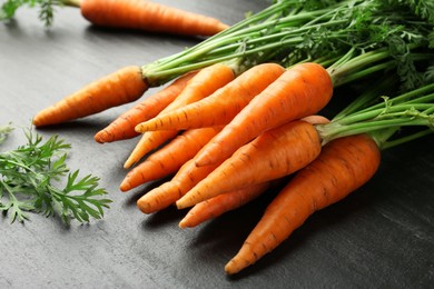 Photo of Tasty ripe juicy carrots on dark gray textured table, closeup