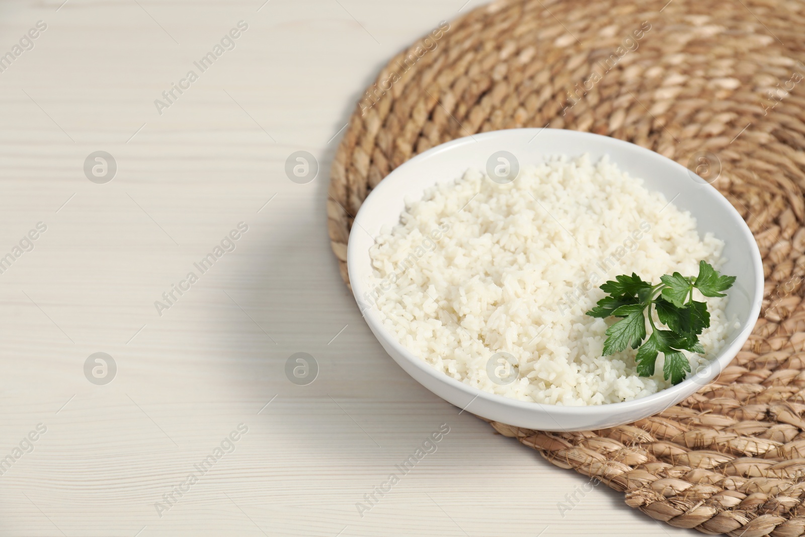 Photo of Delicious boiled rice in bowl and parsley on wooden table, space for text