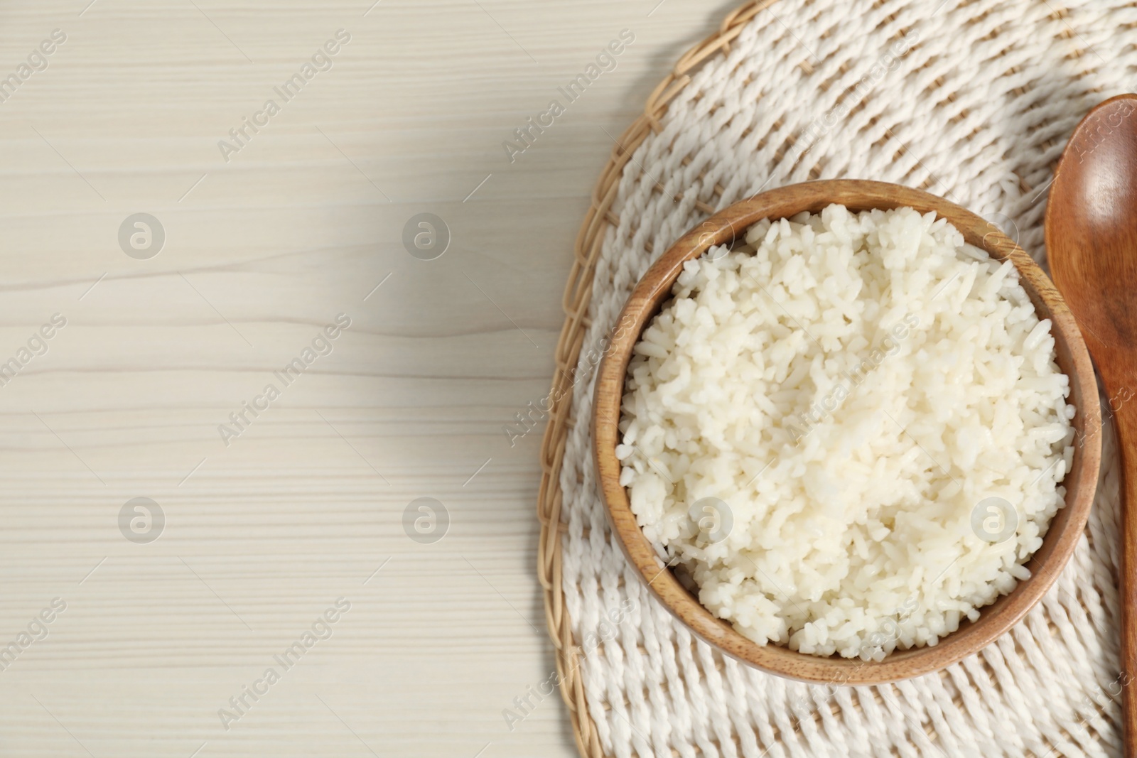 Photo of Delicious boiled rice in bowl and spoon on wooden table, top view. Space for text