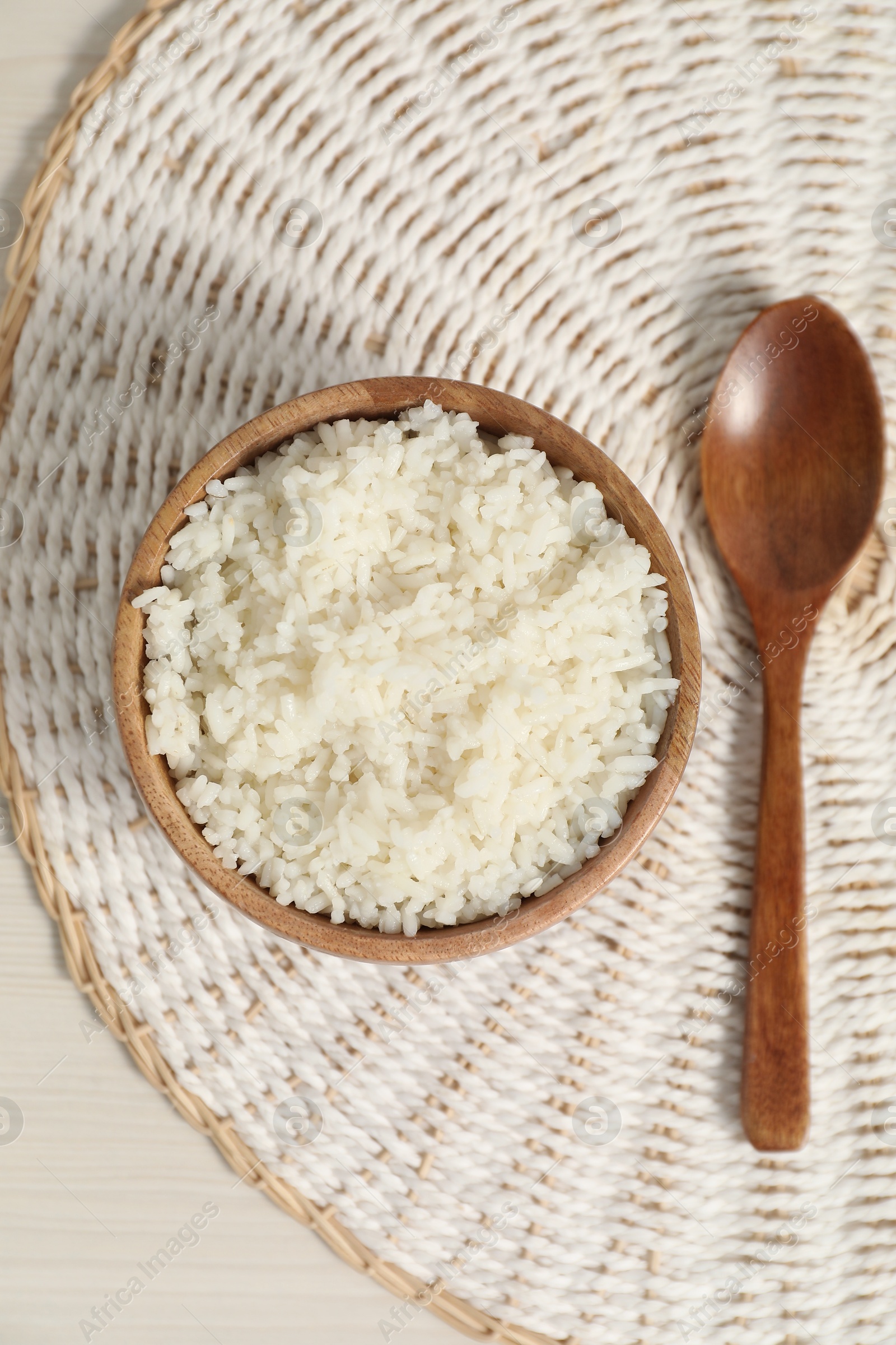 Photo of Delicious boiled rice in bowl and spoon on wooden table, top view