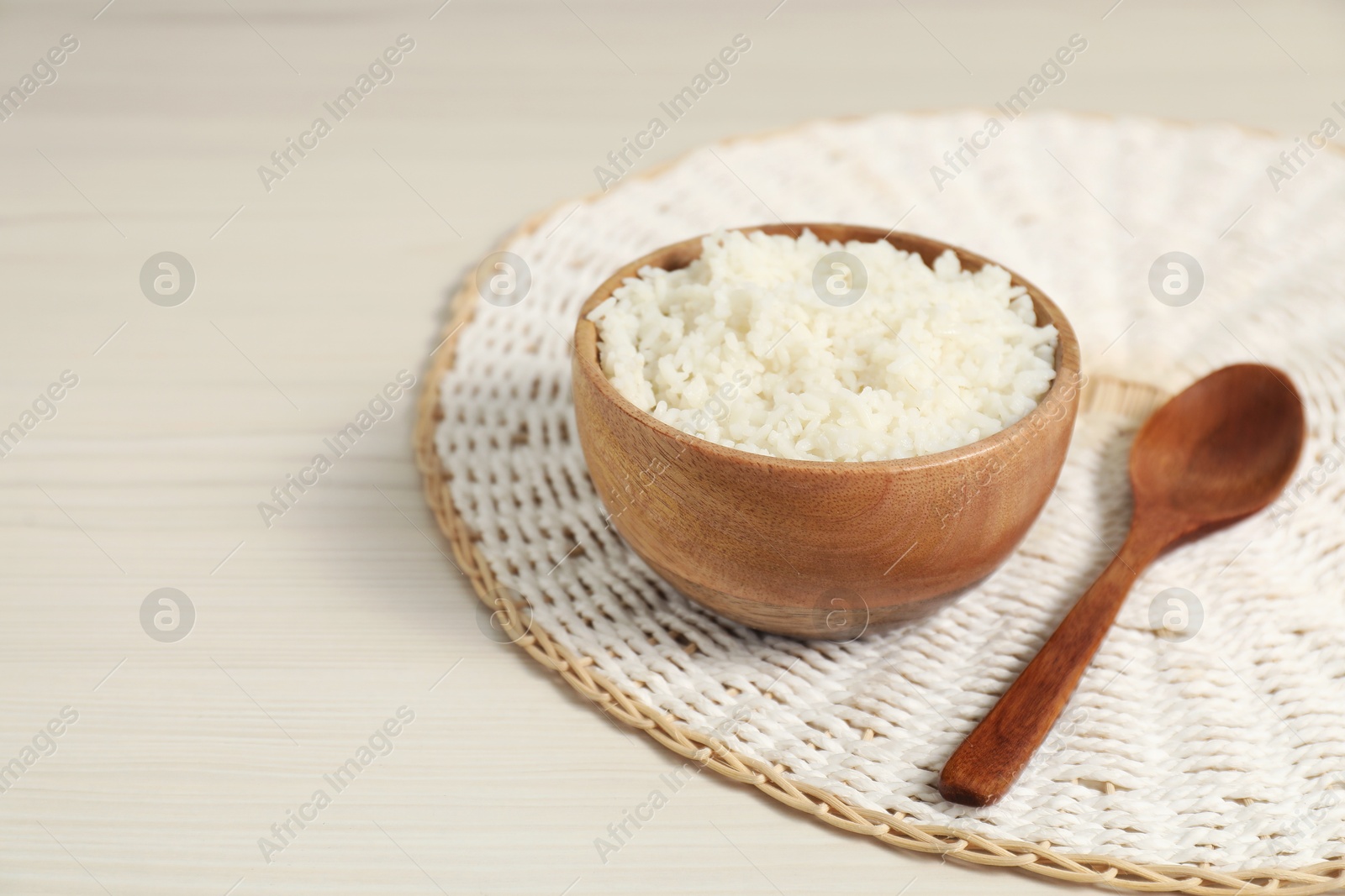 Photo of Delicious boiled rice in bowl and spoon on wooden table, space for text