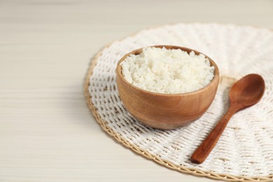 Photo of Delicious boiled rice in bowl and spoon on wooden table, space for text