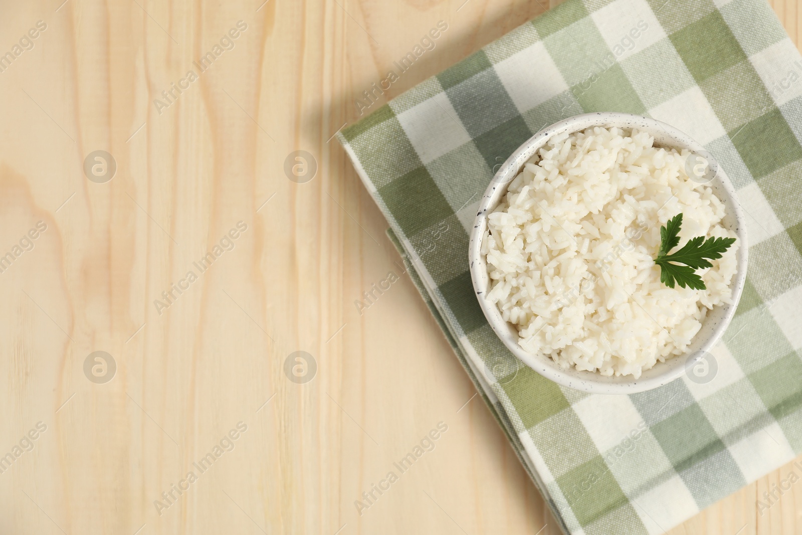 Photo of Delicious boiled rice in bowl and parsley on wooden table, top view. Space for text