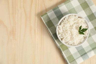 Delicious boiled rice in bowl and parsley on wooden table, top view. Space for text