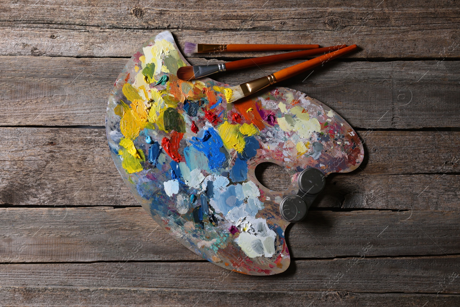 Photo of Artist's palette, brushes and paints on wooden table, flat lay