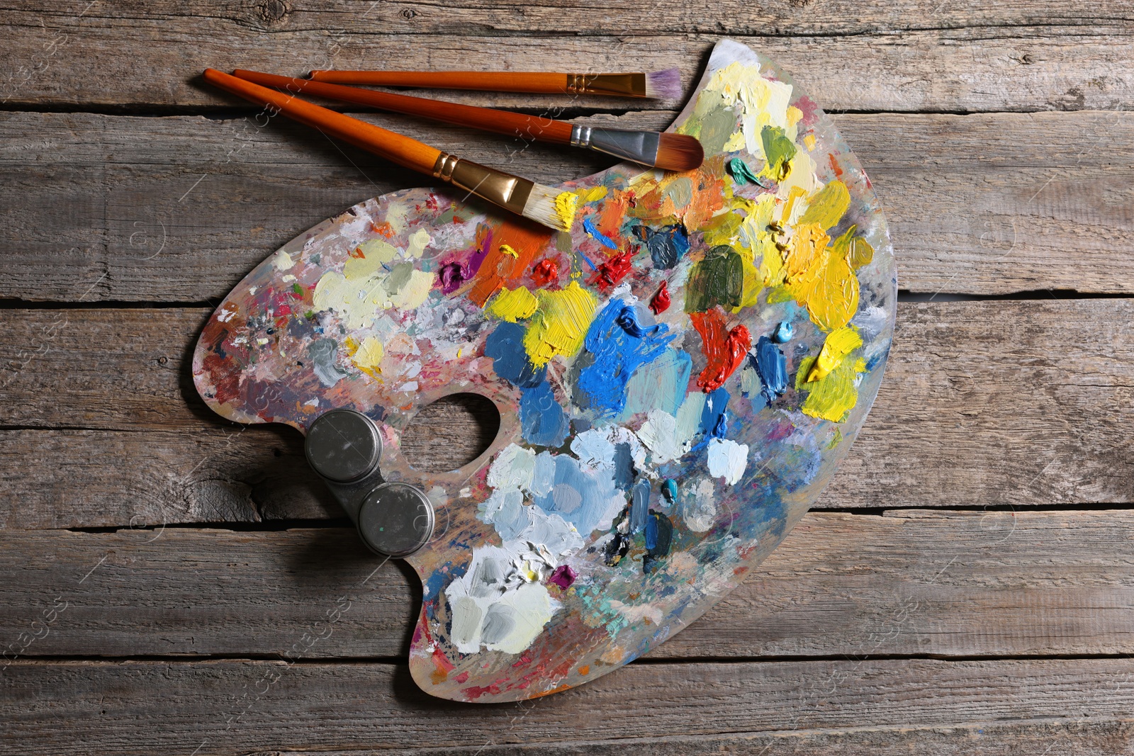 Photo of Artist's palette, brushes and paints on wooden table, flat lay