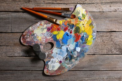 Photo of Artist's palette, brushes and paints on wooden table, flat lay