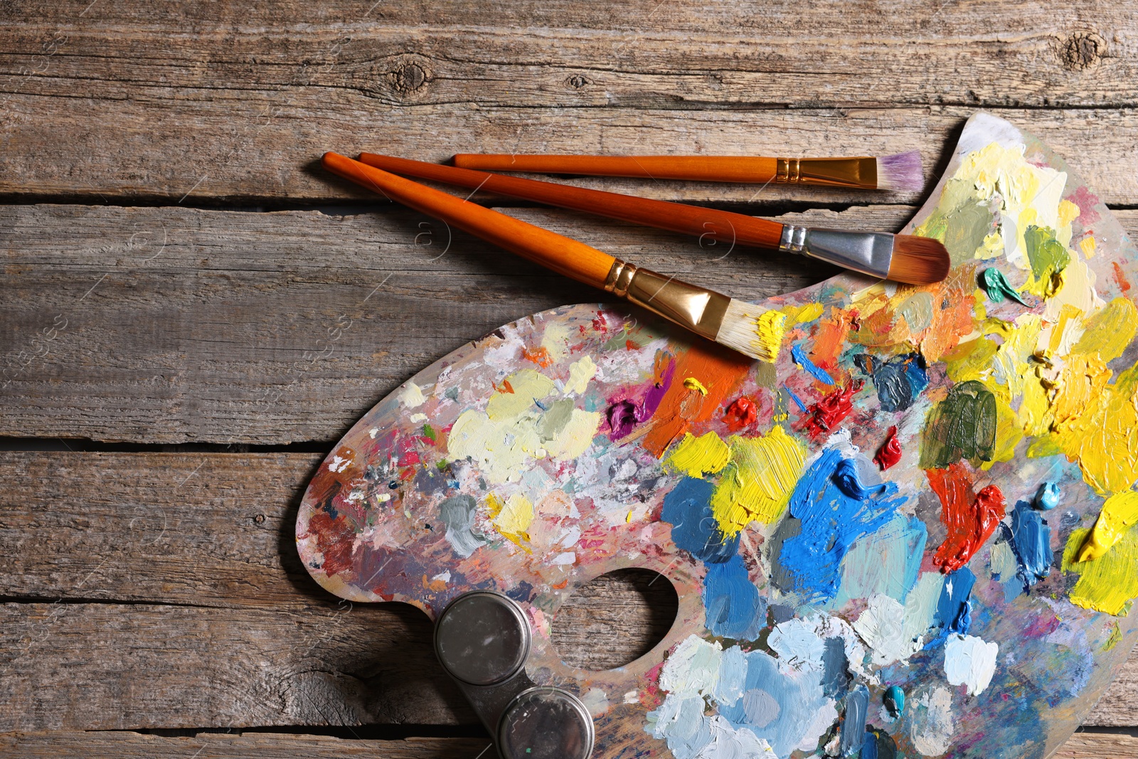 Photo of Artist's palette, brushes and paints on wooden table, flat lay. Space for text