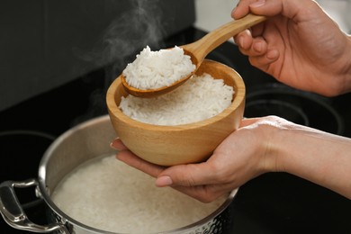 Photo of Woman taking boiled rice from pot into bowl, closeup