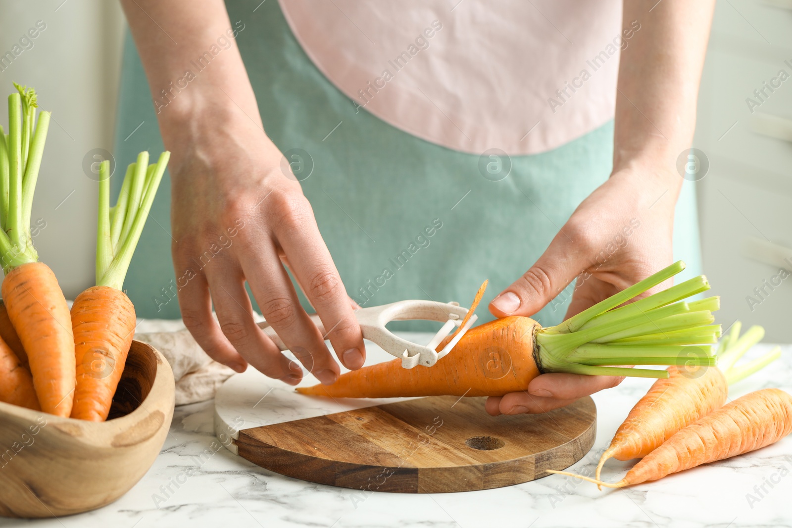 Photo of Woman peeling fresh carrot at white marble table, closeup