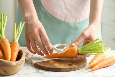 Photo of Woman peeling fresh carrot at white marble table, closeup