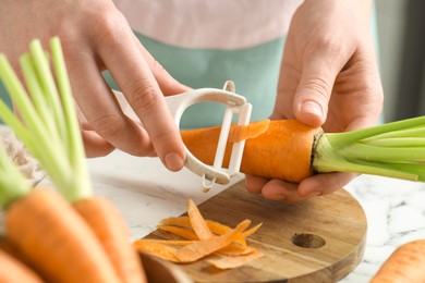 Woman peeling fresh carrot at white marble table, closeup