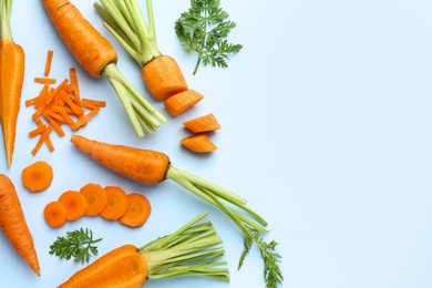 Photo of Whole and cut fresh carrots with green leaves on light background, flat lay. Space for text