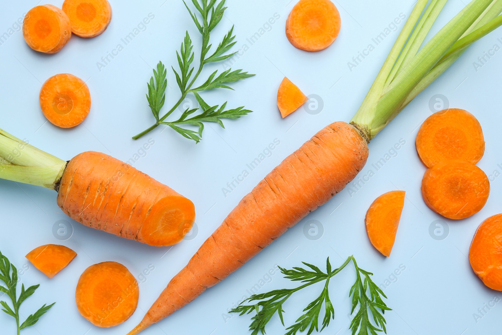 Photo of Whole and cut fresh carrots with green leaves on light background, flat lay