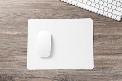 Photo of Computer mouse with mousepad and keyboard on wooden desk, top view