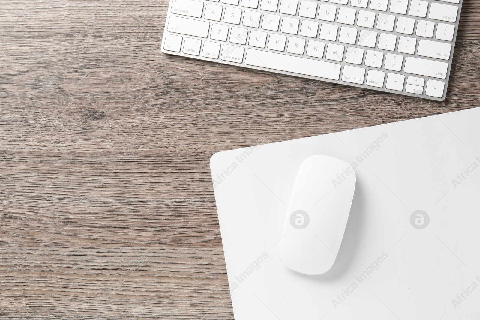 Photo of Computer mouse with mousepad and keyboard on wooden desk, top view. Space for text