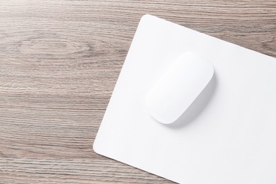 Photo of Computer mouse with mousepad on wooden desk, top view. Space for text