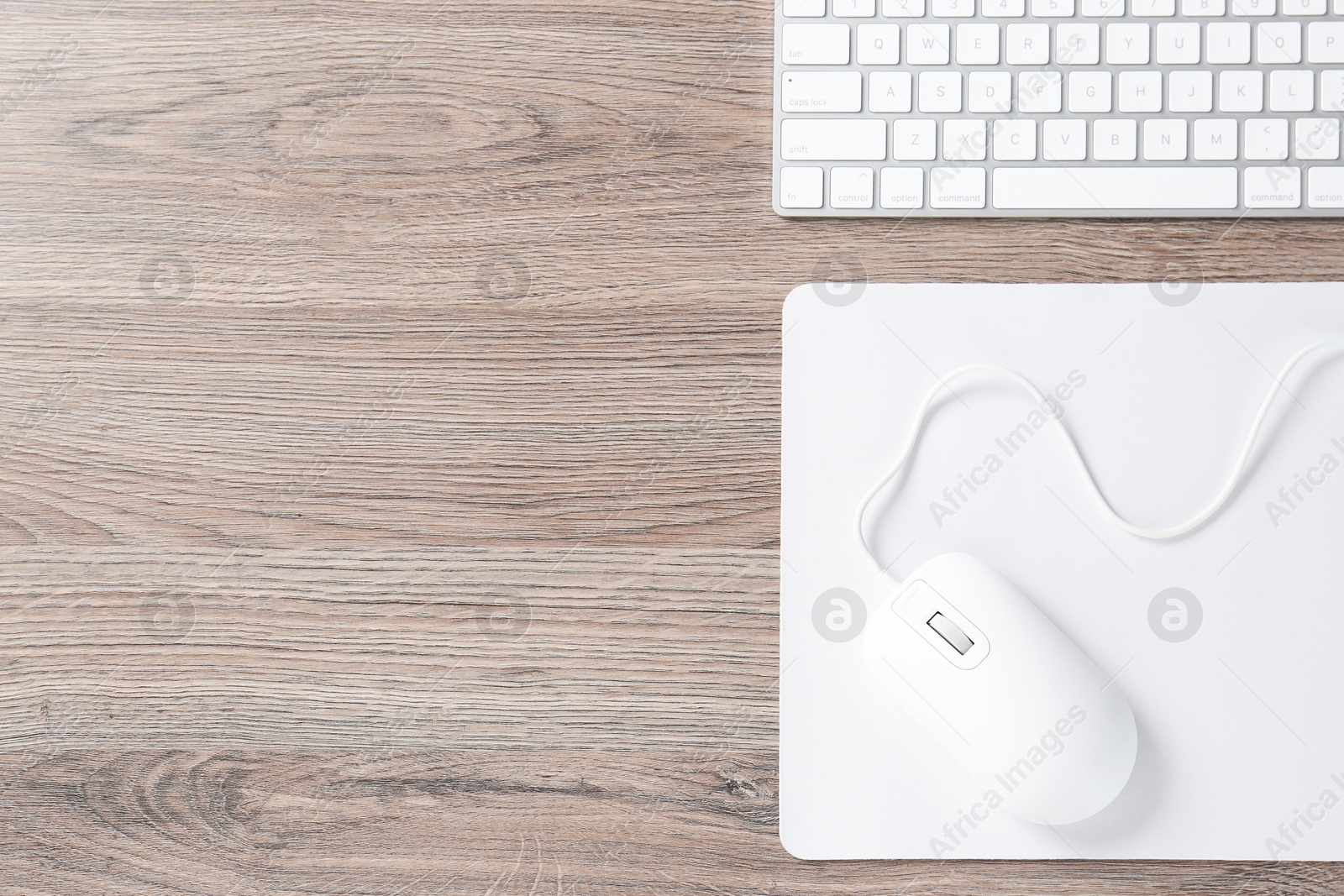 Photo of Computer mouse with mousepad and keyboard on wooden desk, top view. Space for text