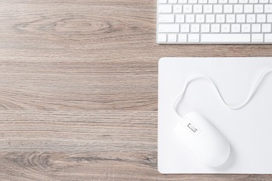 Photo of Computer mouse with mousepad and keyboard on wooden desk, top view. Space for text