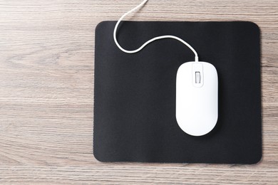 Photo of Computer mouse with mousepad on wooden desk, top view