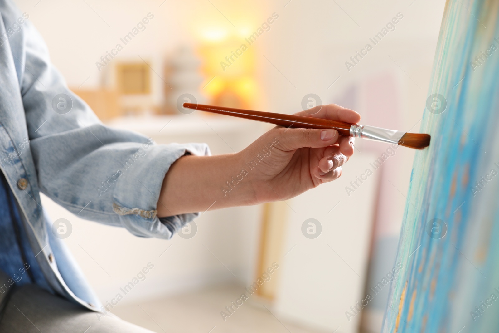 Photo of Woman painting on easel with canvas indoors, closeup