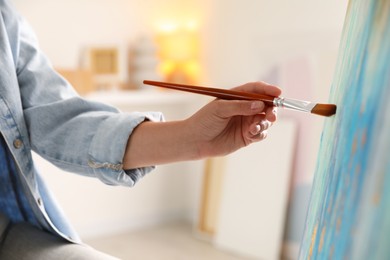 Woman painting on easel with canvas indoors, closeup