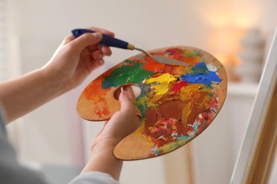 Woman with knife using palette near easel indoors, closeup