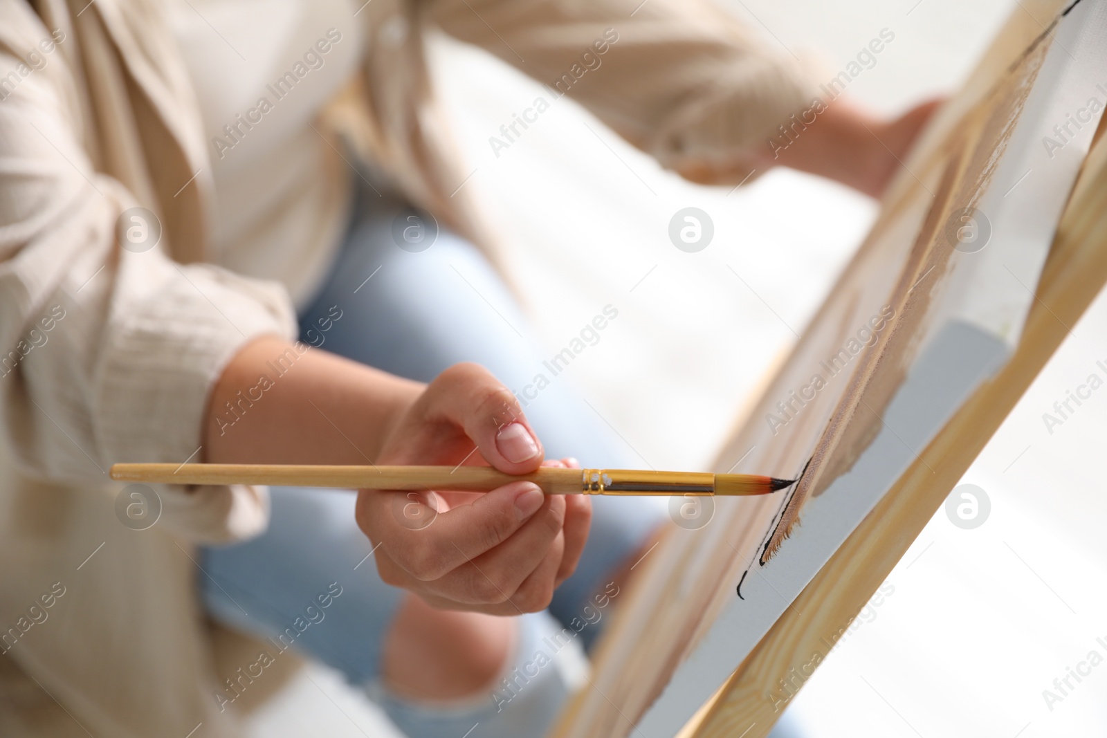 Photo of Woman painting on easel with canvas indoors, closeup