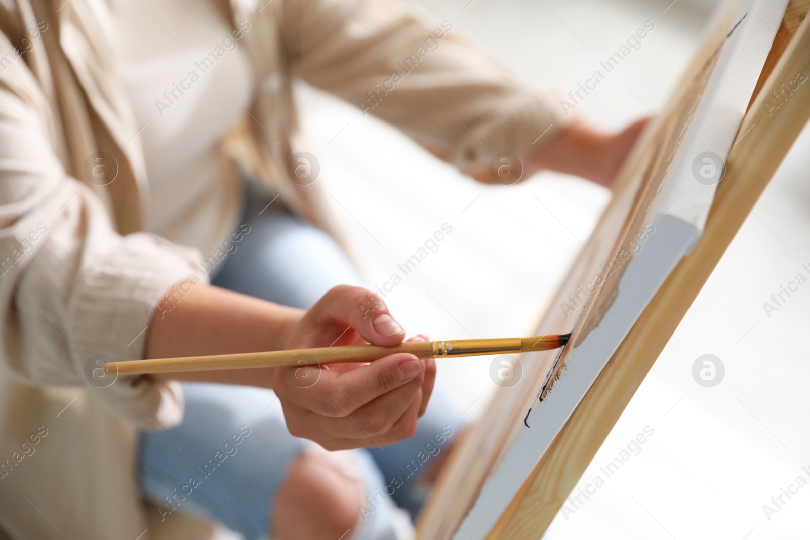 Photo of Woman painting on easel with canvas indoors, closeup