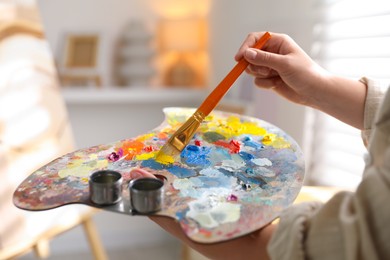 Photo of Woman mixing paints on palette with brush indoors, closeup