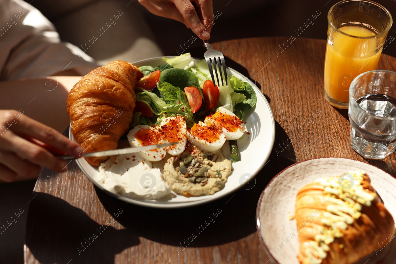 Photo of Woman having tasty breakfast at wooden table in cafe, closeup