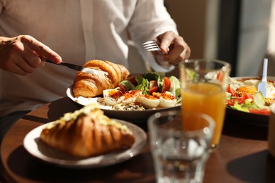 Photo of Man having tasty breakfast at wooden table in cafe, closeup