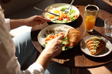 Photo of Man having tasty breakfast at wooden table in cafe, closeup