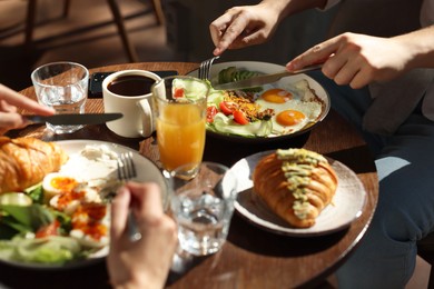 Photo of Couple having tasty breakfast at wooden table in cafe, closeup