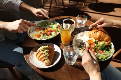 Photo of Couple having tasty breakfast at wooden table in cafe, closeup