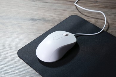 Photo of Computer mouse with mousepad on wooden table, closeup