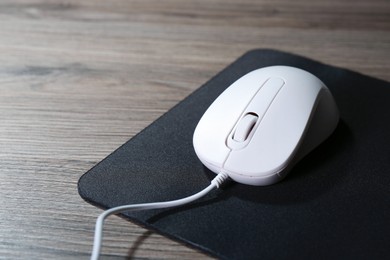 Photo of Computer mouse with mousepad on wooden table, closeup. Space for text