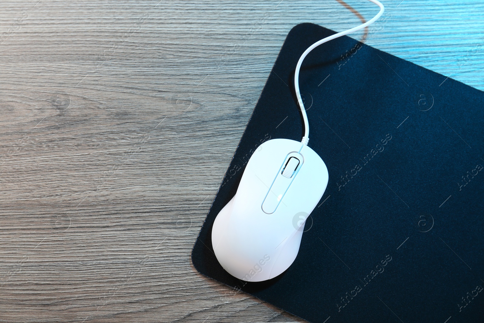 Photo of Computer mouse with mousepad on wooden table, top view. Space for text