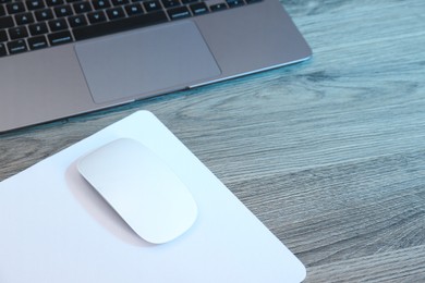 Photo of Computer mouse with mousepad and laptop on wooden table. Space for text