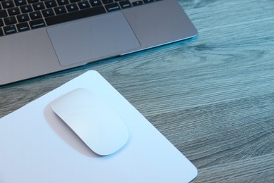 Photo of Computer mouse with mousepad and laptop on wooden table. Space for text