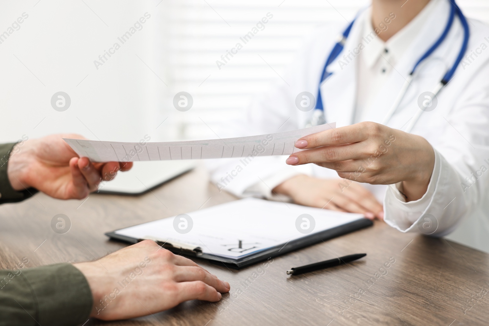 Photo of Doctor giving prescription to patient at wooden table in clinic, closeup