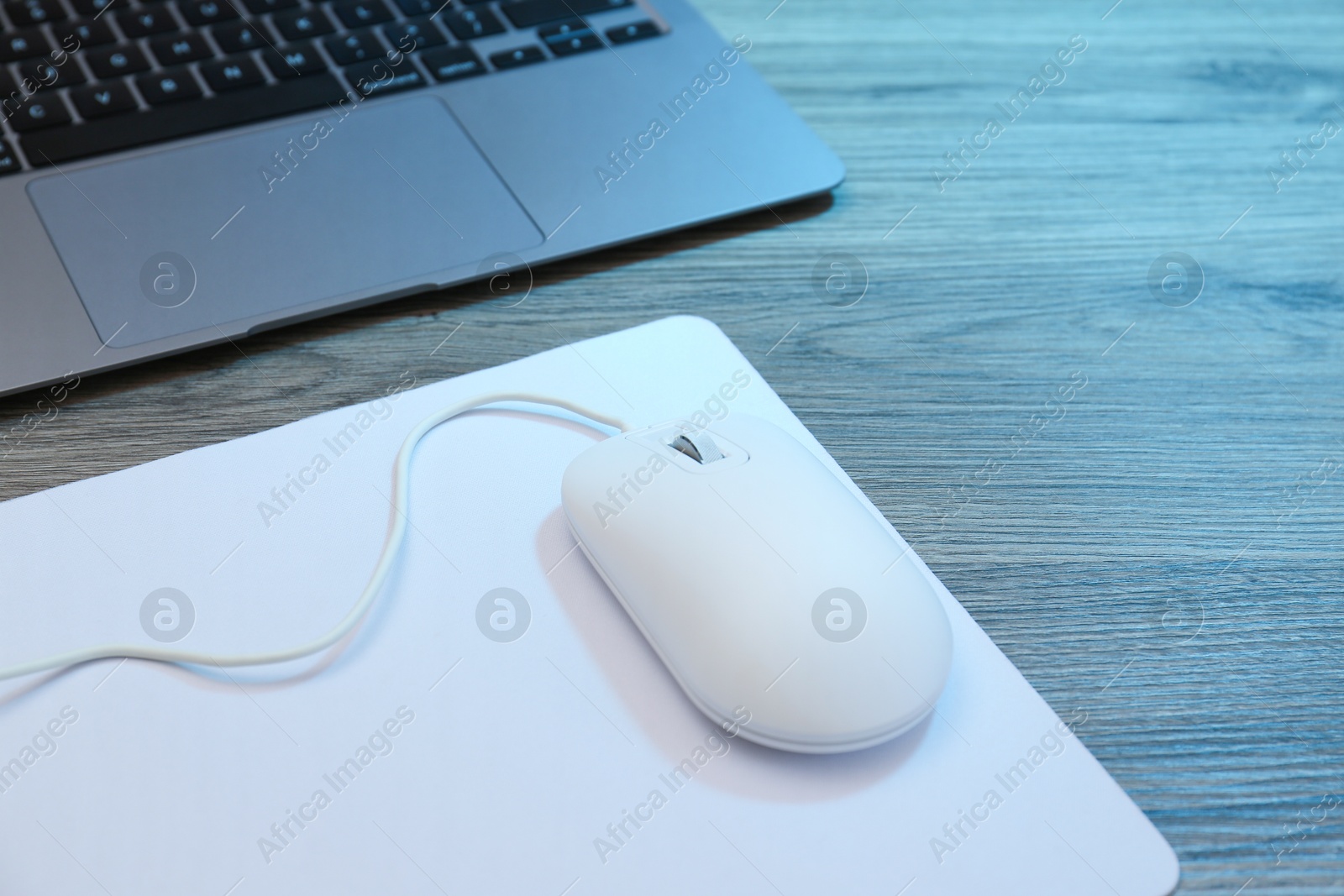 Photo of Computer mouse with mousepad and laptop on wooden table