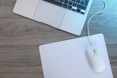 Photo of Computer mouse with mousepad and laptop on wooden table, flat lay