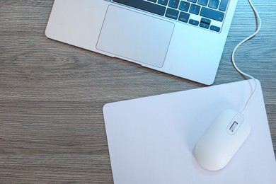 Photo of Computer mouse with mousepad and laptop on wooden table, flat lay