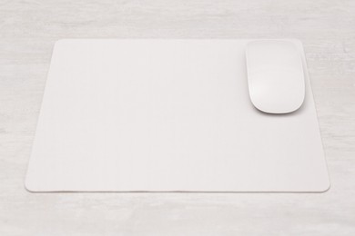 Photo of Computer mouse with mousepad on light wooden table